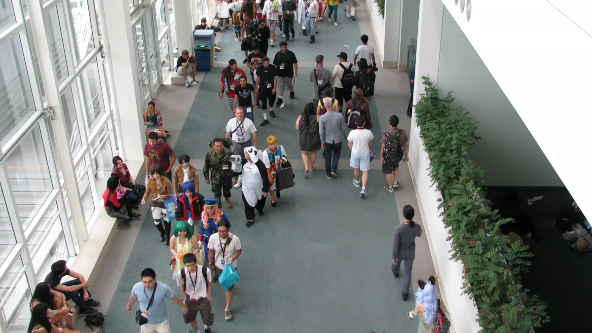 Convention Center Hallway Foot Traffic attendees with badges and backpacks walking a long convention center hallway between halls